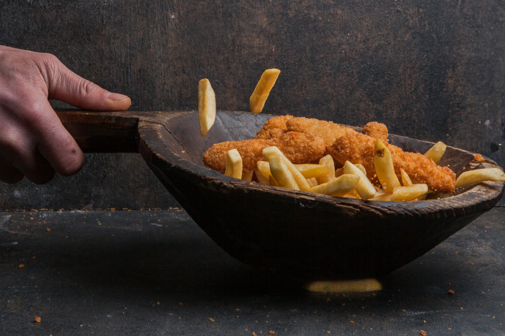 A wooden bowl of golden-brown chicken nuggets served with crispy French fries