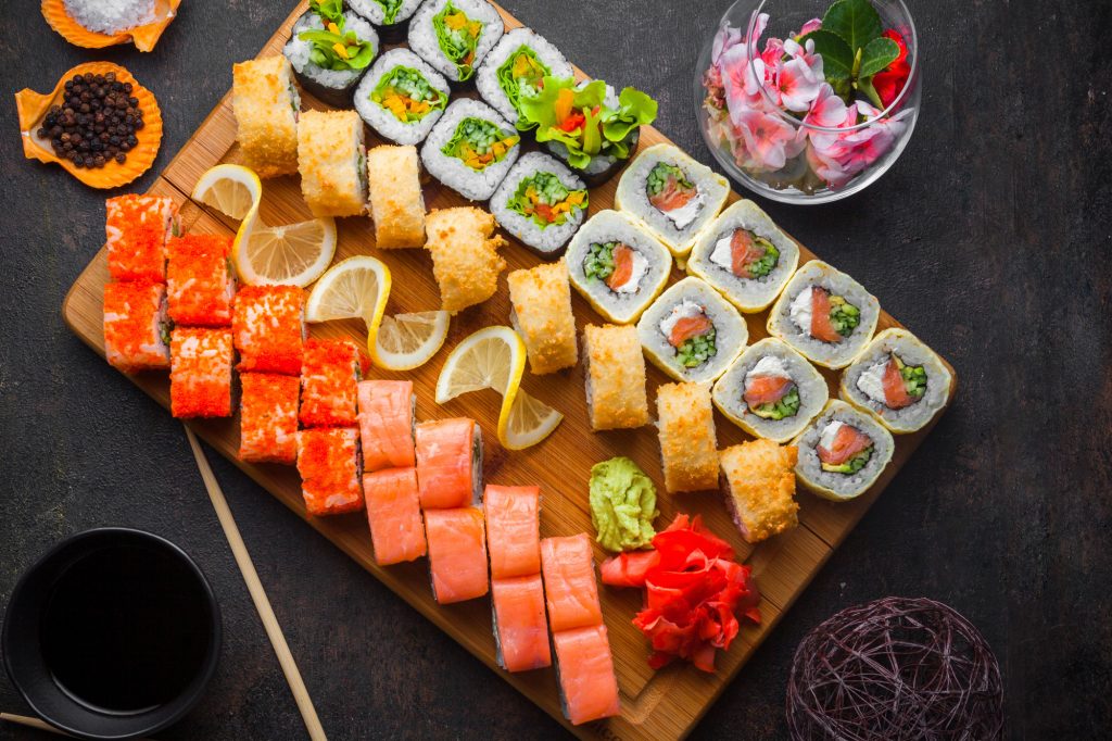 A wooden serving board featuring an array of colorful sushi rolls, nigiri, and sashimi, beautifully arranged with pickled ginger, wasabi, and soy sauce on the side